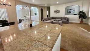 A spacious living area with a large granite island, a sectional sofa, and a flat-screen TV mounted on the wall. - Modern and Stylish Retreat with Game Room (Tigard)