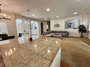 A spacious living area with a large granite island, a sectional sofa, and a flat-screen TV mounted on the wall.