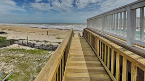 A wooden boardwalk leading to a beach with a clear sky. - Oceans Edge (Galveston)