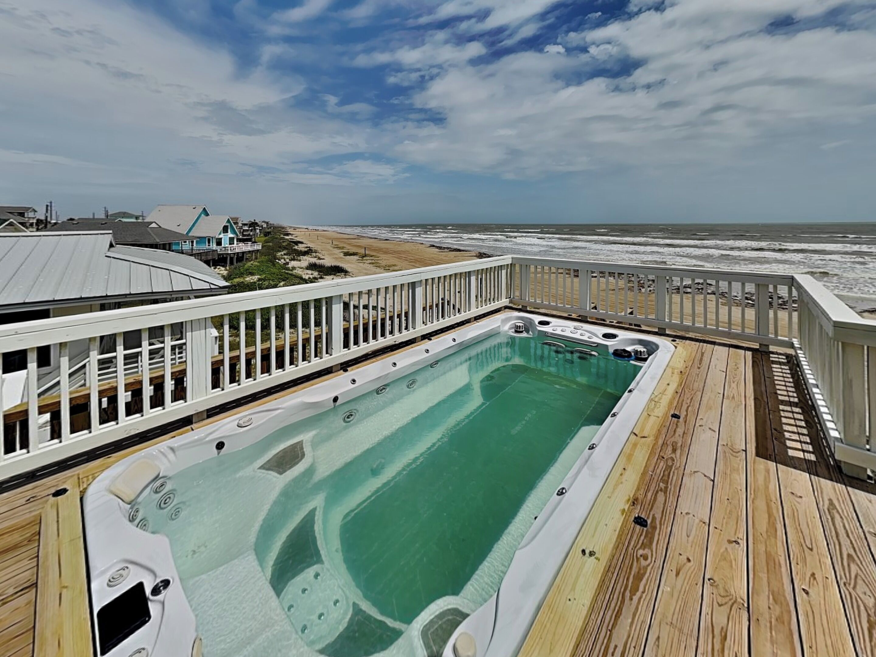 A wooden deck with a hot tub overlooking a beach.