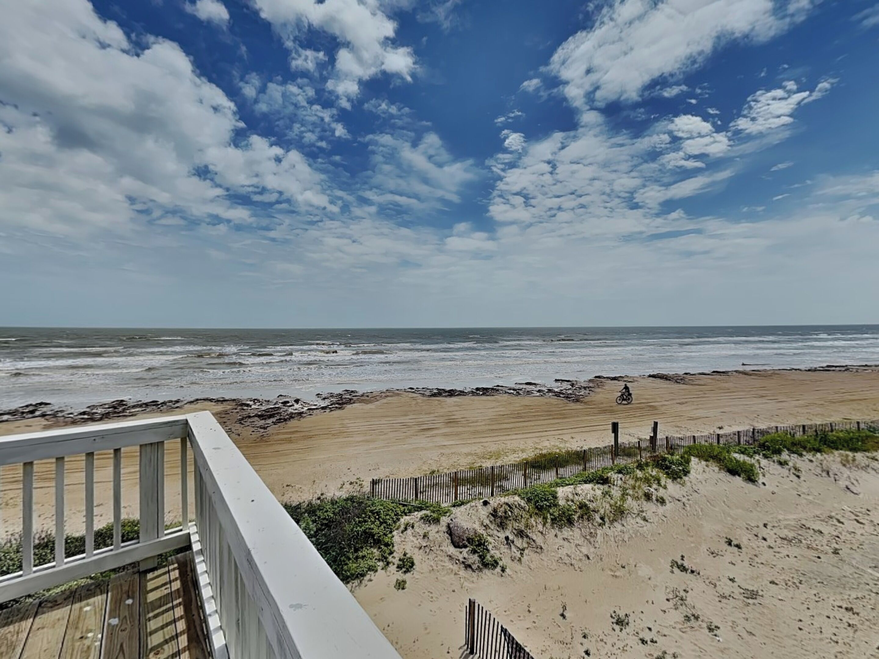 A beach view with a wooden deck and a fence.