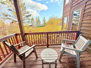 A wooden deck with two chairs and a small table, overlooking a forested area with autumn foliage. - Tranquil Hillside Lower 2BR Condo in Lutsen (Lutsen)