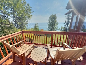 Une terrasse en bois avec une table et des chaises, donnant sur une étendue d’eau et des arbres.
