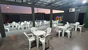 Un espace extérieur aménagé en terrasse, avec des chaises et des tables en plastique blanc, une aire de jeux en arrière-plan et un mur végétal.