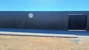 Une façade d’immeuble avec un grand portail noir, une enseigne circulaire et un trottoir dallé.