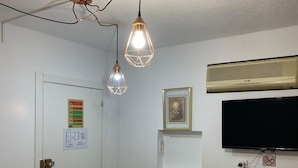 Una habitación con una puerta blanca, aire acondicionado instalado, un cuadro en la pared y un televisor.