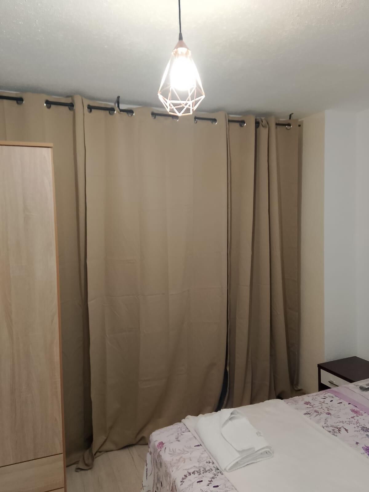 Ein Schlafzimmer mit Bett, Vorhängen, einem Holzschrank und einer Pendelleuchte.