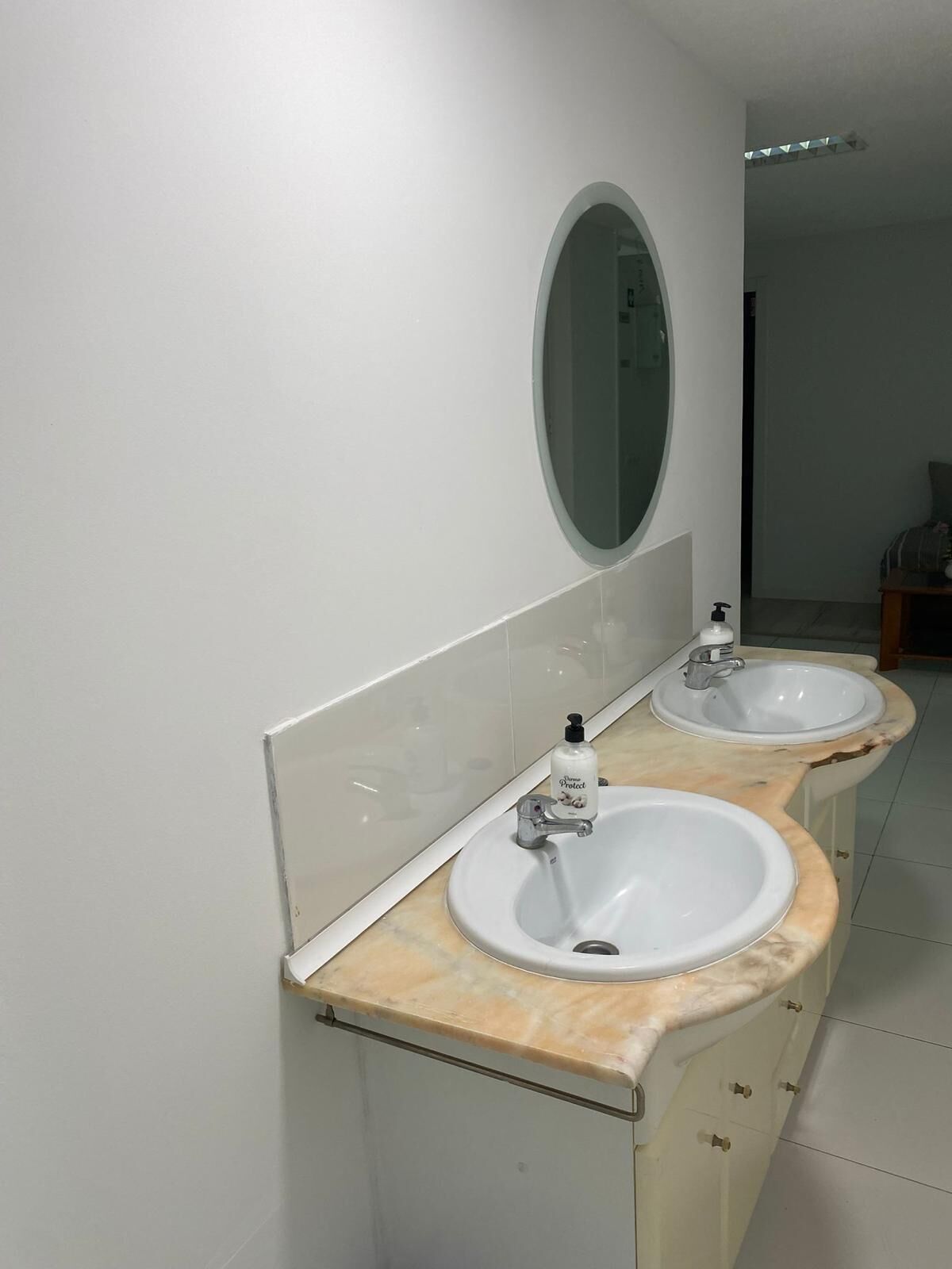 A bathroom with two sinks, a mirror, and a bottle of hand soap.