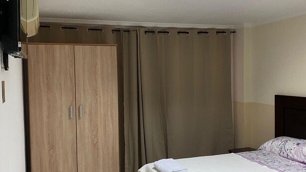 Un dormitorio con cama, armario, televisor y tragaluz.