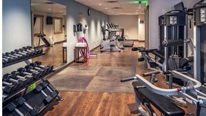 Ein Fitnessraum mit Trainingsgeräten, einem Spiegel und Holzboden.