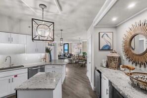 A modern kitchen with granite countertops, white cabinetry, and a central island. - Beachfront Corner Unit Condo | Pool | Sleeps 6 (Orange Beach)