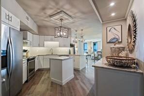 A modern kitchen with a central island, stainless steel appliances, and a dining area with a view. - Beachfront Corner Unit Condo | Pool | Sleeps 6 (Orange Beach)