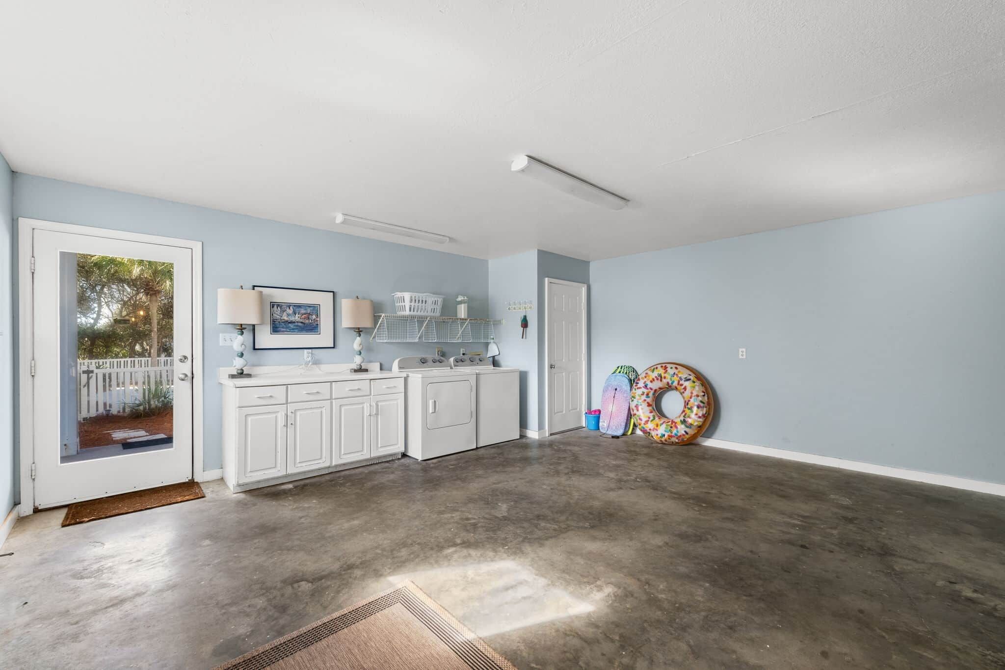 A spacious laundry room with a concrete floor, white cabinets, a washing machine, a dryer, and a door leading outside.