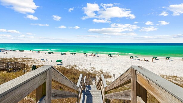 Een houten trap die uitkomt op een strand met helder turquoise water en een heldere lucht.