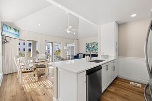 A modern kitchen with white cabinetry, a central island, and a built-in dishwasher. - A Perfect Summer East (Walton County)