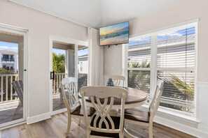 A dining area with a table and chairs, a TV mounted on the wall, and a view of the ocean through large windows. - A Perfect Summer West (Walton County)