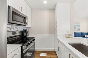 A modern kitchen with white cabinetry, a black stove, and a microwave. - A Perfect Summer West (Walton County)