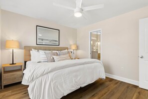 A bedroom with a bed, nightstands, a ceiling fan, a framed picture, and a door. - A Perfect Summer West (Walton County)