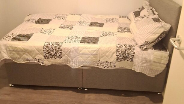 Ein Bett mit einer Steppdecke, einem Kopfteil und einem Holzboden.