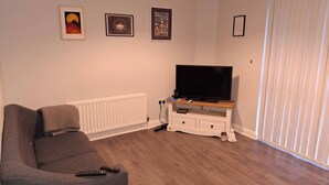 Ein Wohnzimmer mit einer Couch, einem Fernseher auf einem Holzboden und einer Heizung.