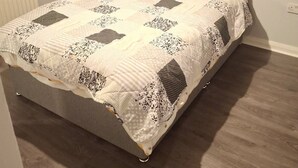 Ein Bett mit grauem Kopfteil, einem gemusterten Quilz und zwei Kissen.