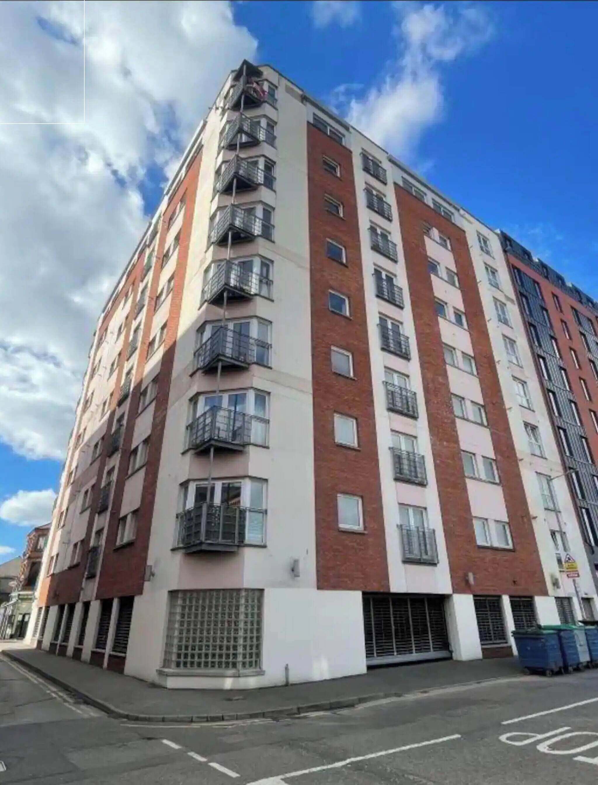 A multi-story residential building with balconies, a gated entrance, and a clear sky.