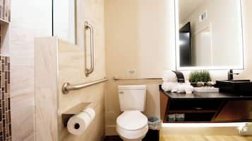 A bathroom with a toilet, a handrail, a towel rack, a mirror, and a sink with a countertop.