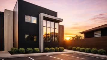 A modern building with a parking lot, large windows, and a sunset in the background.
