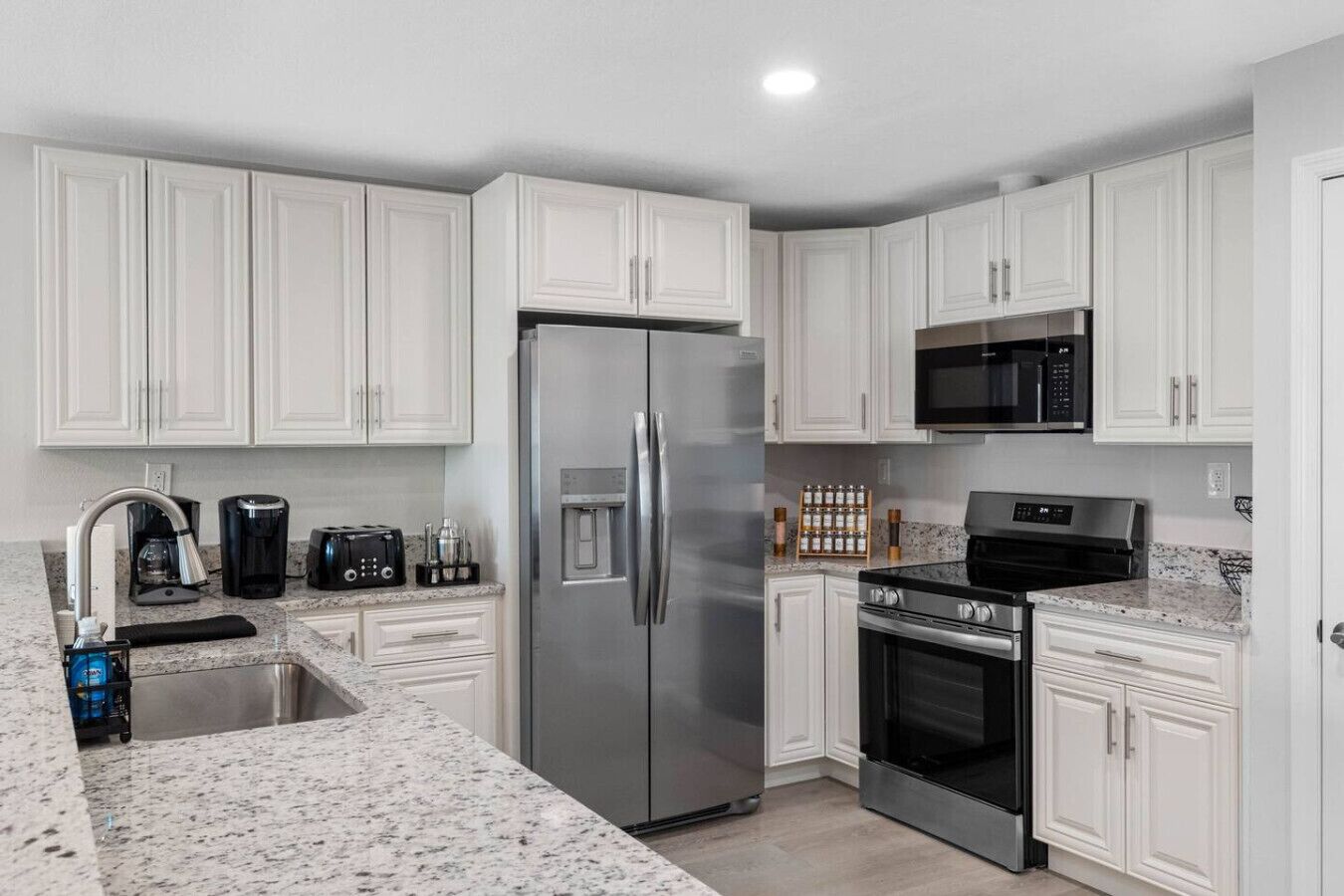 A kitchen with white cabinets, a stainless steel refrigerator, a microwave, a stove, and a coffee maker.