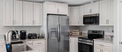 A kitchen with white cabinets, a stainless steel refrigerator, a microwave, a stove, and a coffee maker.