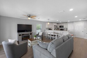 A modern living room with a flat-screen TV, grey sofa, and a dining area with white chairs. - Spacious Waterfront Home Near Downtown Tampa (Tampa)