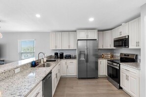 A modern kitchen with white cabinets, stainless steel appliances, granite countertops, and a window with blinds. - Spacious Waterfront Home Near Downtown Tampa (Tampa)