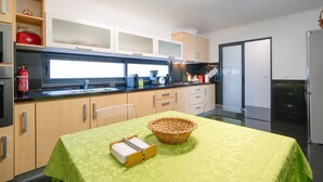 A modern kitchen with wooden cabinets, a stainless steel refrigerator, and a dining table with a green tablecloth. - Ponta do Sol Apartment | Three-Bedroom (Ponta do Sol)
