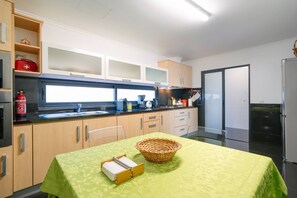 A modern kitchen with wooden cabinets, a stainless steel refrigerator, and a dining table with a green tablecloth. - Ponta do Sol Apartment | Three-Bedroom (Ponta do Sol)