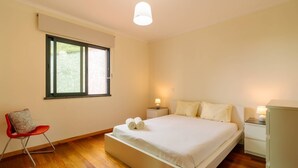 A bedroom with a large bed, a chair, bedside tables, and a window. - Ponta do Sol Apartment | Three-Bedroom (Ponta do Sol)