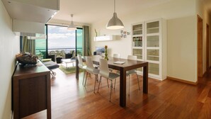 A modern dining area with a wooden table, white chairs, and pendant lighting. - Ponta do Sol Apartment | Three-Bedroom (Ponta do Sol)