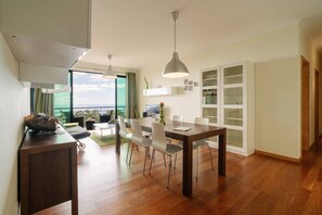 A modern dining area with a wooden table, white chairs, and pendant lighting. - Ponta do Sol Apartment | Three-Bedroom (Ponta do Sol)
