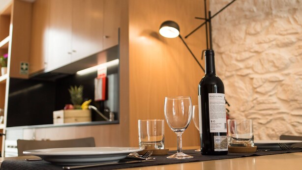 Spisebord med vinflaske, glas og bestik foran en væg med struktur og en moderne lampe.