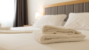 Een net opgemaakt bed met witte lakens en een opgevouwen handdoek aan de zijkant.