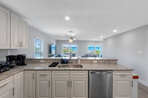 A kitchen with white cabinets, a granite countertop, a dishwasher, and a ceiling fan. - Brand-New Waterfront Retreat Near Tampa Bay (Tampa)