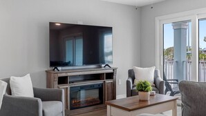 Ein Wohnzimmer mit Flachbildfernseher, Kamin, grauen Sofas und einem Balkon mit Blick.