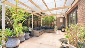 Eine überdachte Terrasse mit Ecksofa, Kübelpflanzen und Grillbereich.