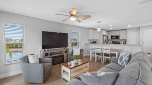 Un salon moderne avec un téléviseur à écran plat, des canapés gris, une table basse et un ventilateur de plafond.