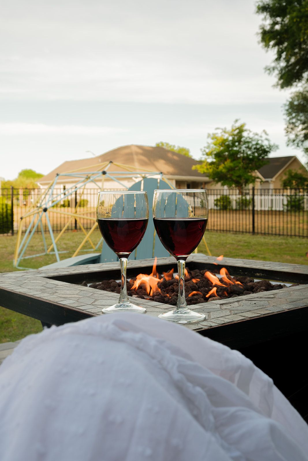 Two glasses of red wine on a table with a fire pit in the background.
