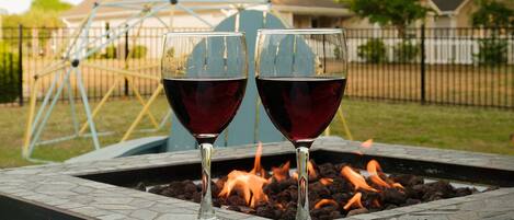 Two glasses of red wine on a table with a fire pit in the background.