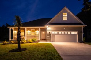 Uma casa de dois andares com varanda coberta, garagem e um jardim frontal bem iluminado.
