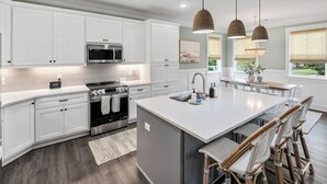 Una cocina moderna con armarios blancos, una isla central, horno empotrado e iluminación colgante.