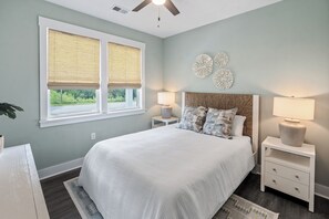 Quarto com cama, duas mesas de cabeceira, ventilador de teto e janela com persianas.