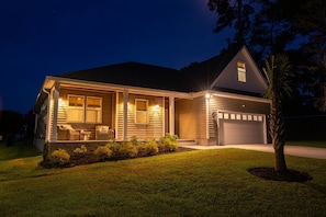 A residential house with a covered porch, a garage, and a well-maintained lawn. - Coastal Retreat~Ocean Isle Beach. Relax by Fire Pit, with beautiful Pond View. (Ocean Isle Beach)