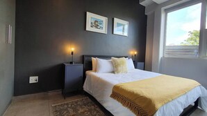 A bedroom with a bed, bedside tables, a desk, and a window. - 15 Sunny 1-bedroom Apartment (Johannesburg)